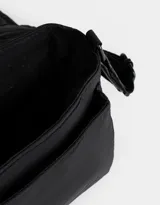 Bandolera negra de tela deportiva con correa regulable y desmontable, solapa con broche a presión y hebilla frontal con estampa.