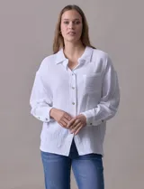 Camisa blanca de algodón con textura arrugada, cuello con solapa, abertura central con botones y bolsillo aplicado en el pecho. Mangas largas con largo regulable mediante presilla y botón.