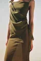 Falda larga color verde oliva, de tiro medio y corte recto. Presenta una superposición de tela tipo pareo ajustable con lazadas.