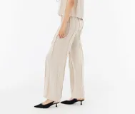 Pantalón de lino color beige, de corte recto y tiro alto, con detalle de flecos verticales.