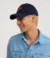 Gorra de sarga de algodón color marrón oscuro con visera curva y ajuste trasero. Presenta un bordado frontal con las letras 'NYC' en estilo universitario con detalles en rojo y blanco, flanqueadas por los números '19' y '86' y tres estrellas blancas debajo.