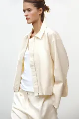 Cazadora tipo bomber color crema confeccionada en hilatura con mezcla de algodón. Cuello solapa y manga larga. Bolsillos delanteros. Forro interior a tono. Bajo ajustable. Cierre frontal con cremallera metálica.