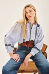 Camisa celeste de voile con bordados en negro en el frente, mangas y cuello. Tiene corte amplio, escote redondo y cartera delantera con botones.