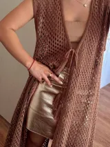 Chaleco largo tejido con hilo de algodón y lurex color marrón, en punto calado tipo red con escote profundo en V, tiras para atar, tajo trasero y flecos en el ruedo.