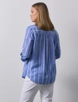 Camisa color beige con rayas verticales blancas, de lino, con cuello con solapa y abertura central con botones. Tiene un bolsillo aplicado en el pecho y mangas largas regulables con presilla y botón.