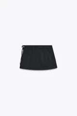 Falda pantalón negra de tiro alto con aberturas laterales y cierre cruzado con lazadas y cremallera oculta.