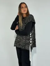 Chaleco de punto con diseño jaspeado en tonos grises y negros, con cordones blancos cruzados en los laterales.