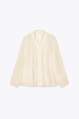 Camisa color crema de algodón con cuello redondo, escote pico con lazadas, manga larga con puños y cierre frontal con botones.