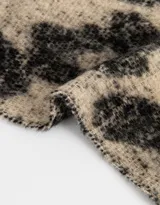 Bufanda tejida de lana en tonos beige y negro, con estampado geométrico y terminación en flecos.