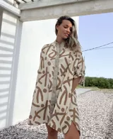 Vestido camisero de lino color beige con estampado abstracto en marrón. Tiene cuello camisero, cierre frontal con botones y mangas 3/4 con trabillas.