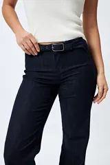 Pantalón de jean azul oscuro, de corte flare con cinturón incorporado en la misma tela y silueta ajustada en cadera que se ensancha hacia el ruedo.