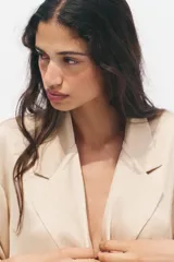Blazer color beige de cuello solapa y manga tres cuartos. Tejido con efecto arrugado y cierre frontal cruzado con botones negros.