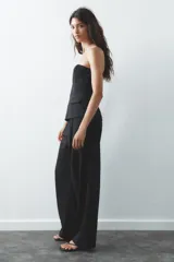 Top blanco de escote recto con detalle de pieza metálica en forma de V forrada y hombros descubiertos. Tiene falsos bolsillos con solapa en el delantero, forro interior combinado y cierre lateral con cremallera oculta en la costura.