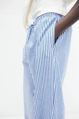 Pantalón de corte holgado en algodón a rayas verticales azules y blancas. Modelo de tiro alto con cintura elástica fruncida y cordón para ajustar. Piernas anchas con bolsillos laterales discretos.