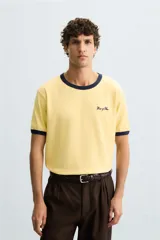 Camiseta amarilla de corte regular fit, cuello redondo y manga corta. Tiene un bordado frontal de texto en color azul marino. Acabados con rib a contraste en cuello y mangas.