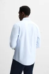 Camisa celeste a rayas verticales blancas, de corte recto, con cuello italiano abierto, manga larga con puños abotonados y cierre frontal con botones.