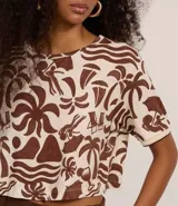 Blusa tipo t-shirt de corte super cropped con cuello redondo y mangas cortas. Presenta un estampado de íconos playeros en color marrón sobre un fondo beige.