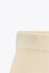 Minifalda color crema de punto liso, tiro alto, cintura elástica y corte evasé.