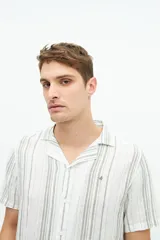 Camisa de manga corta confeccionada en lino y algodón a rayas verticales en tonos blanco, gris y beige. Tiene cuello tipo cubano, corte regular y logo bordado en el pecho.
