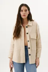 Sobrecamisa color beige de lino con cuello camisero, cierre frontal con botones negros, mangas largas con puños abotonados, dos bolsillos de parche en el pecho y dos bolsillos laterales.