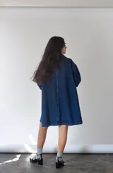 Vestido camisero largo de denim azul con botones frontales, cuello camisero, mangas largas y bolsillos de parche en el pecho.