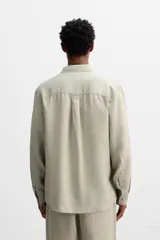 Camisa color arena de lino con cuello abotonado, manga larga con puños abotonados, corte regular y bajo con aberturas laterales.
