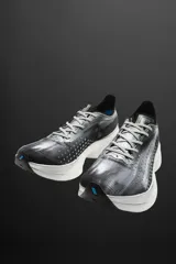 Zapatilla deportiva para correr largas distancias, color gris y negro, con parte superior de tejido de punto transpirable y suela de TPE-A. Cuenta con placa de carbono interna, plantilla interior OrthoLite®, stack de 39 mm y drop de 8 mm. Marca Zara Athleticz.