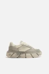 Zapatillas bajas color gris claro con cordones y suela gruesa con diseño irregular.