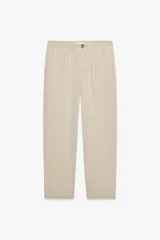 Pantalón color beige de tiro alto con cintura elástica, bolsillos delanteros y falsos bolsillos con solapa en la espalda.