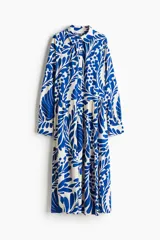 Vestido midi de viscosa con estampado floral azul sobre fondo blanco, cuello camisero, tapeta de botones oculta, mangas raglán largas con puños sencillos y costuras fruncidas en la falda.