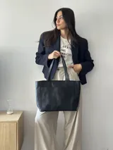 Cartera tipo tote de cuero graneado color negro, con textura uniforme y suave al tacto. Tiene manijas de 55 cm, bolsillo frontal con broche imantado, bolsillo trasero con cierre metálico, cierre principal metálico, forro interior y tres bolsillos internos (uno con cierre, uno plaqué y uno tipo sobre con solapa y botón).