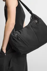 Bolso negro de tela técnica con correa de hombro ajustable. Tiene un compartimento principal con cierre de cremallera, un bolsillo interior con cremallera y tres bolsillos exteriores, uno de ellos con cremallera.