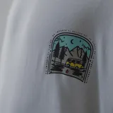 Remera color crema con estampa en la espalda de una combi amarilla en un paisaje de montaña.
