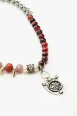 Gargantilla corta con cuentas de diferentes colores y texturas, separadas por piezas metálicas doradas y plateadas. Incluye dije central con forma de escudo plateado.