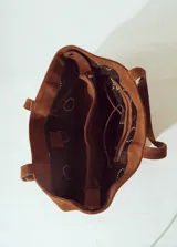 Bolso tipo tote bag de gamuza color marrón, con asas trenzadas y paneles laterales con detalle de trenzado vertical.