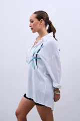 Camisa blanca de corte holgado, con cuello camisero y mangas largas. Decorada con lentejuelas de colores celeste, plateado y negro.