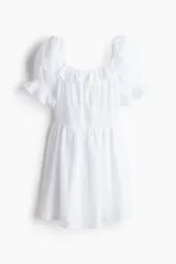 Vestido corto blanco en crepé de algodón con ribete de volado en escote y puños. Modelo con cuerpo ajustado, escote cuadrado y mangas cortas abullonadas. Elástico fino en hombros y escote, y sección fruncida en mangas y cuerpo. Pollera forrada con vuelo.