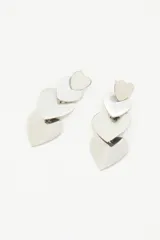 Aretes largos colgantes plateados, compuestos por tres corazones de metal pulido de tamaño decreciente, unidos por argollas.