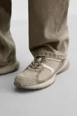 Zapatilla deportiva tipo running de color negro, perteneciente a la colección especial Origins. Presenta una parte superior confeccionada en una combinación de cuero con acabado de gamuza y tejido transpirable. Cuenta con una suela de volumen con diseño irregular y cierre mediante cordones.