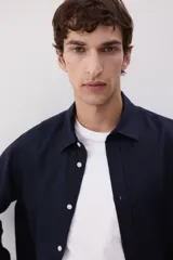 Camisa de hombre de lino color azul marino, de corte regular, con cuello inglés, tapeta clásica, mangas largas con puños abotonados y bajo redondeado.
