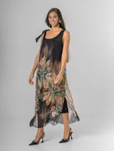 Vestido midi negro con estampado tropical de hojas y flores en tonos tierra, naranja y verde. Es de tirantes anchos con nudo regulable en el hombro y tiene aberturas laterales.
