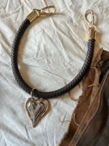 Gargantilla marrón con dije plateado en forma de corazón con borde dorado.