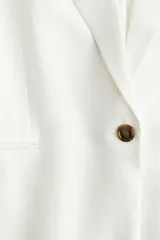 Blazer blanco de lino con solapas de pico, hombreras finas y cierre de un botón. Modelo entallado con pinzas en la cintura, abertura con botón en los puños y bolsillos delanteros ribeteados. Abertura atrás y forro interno.