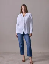 Camisa blanca de algodón con textura arrugada, cuello con solapa, abertura central con botones y bolsillo aplicado en el pecho. Mangas largas con largo regulable mediante presilla y botón.