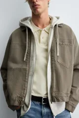 Sobrecamisa de denim de algodón negro con efecto lavado, corte relajado (relaxed fit). Presenta cuello solapa, cierre frontal con cremallera, manga larga con puño abotonado y bolsillo plastrón en el pecho.