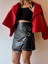 Minifalda negra de ecocuero con diseño cruzado y detalle de argollas metálicas.