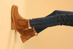 Bota corta color camel de cuero sintético, con detalle de pespuntes negros en el tobillo y cierre lateral con cremallera.