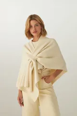 Ruana color crema de tejido de punto industrial con terminación en contraste de color. Tiene doble ojal para mantener el cruce.