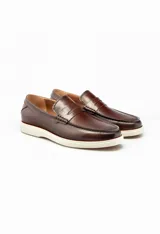 Mocasín de cuero color marrón con antifaz y suela de goma blanca.