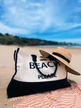Bolso de playa grande de lona color crema con base negra y asas de soga negras. Estampado frontal con la frase "Beach Please" en letras negras.